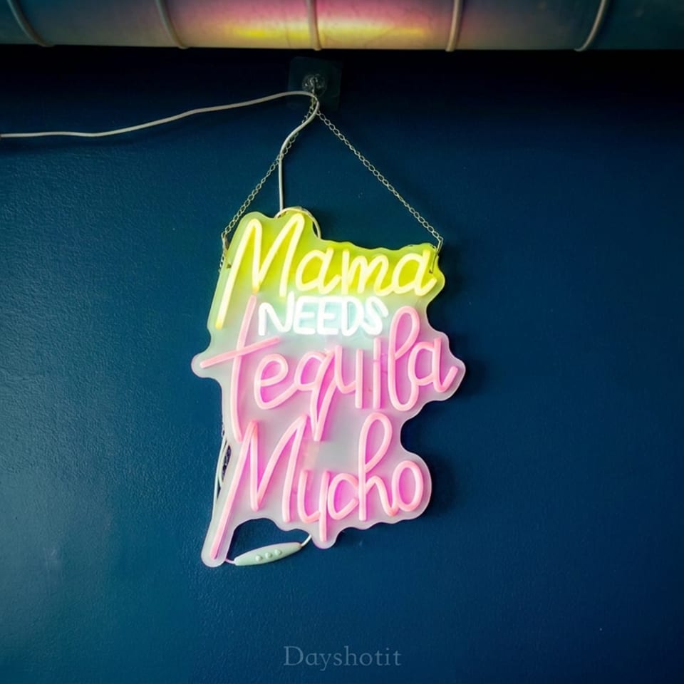 Colorful neon sign reading “Mama Needs Tequila Mucho” hanging on a dark blue restaurant wall.